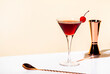 Black Manhattan alcoholic cocktail with whiskey and red vermouth garnished with maraschino cherry in martini glass. Beige background, hard light