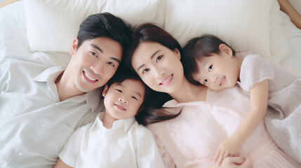 Wall Mural - Happy Asian family lying on bed in bedroom with happy and smile, top view