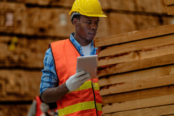 African worker carpenter wearing safety uniform and hard hat working and checking the quality of wooden products at workshop manufacturing. man and woman workers wood in dark warehouse industry.