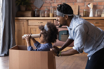 Wall Mural - Smiling African American father with little daughter playing pirates game together, happy family engaged in funny activity on weekend, playful dad and 7s girl having fun in kitchen at home