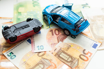 The concept of receipt of insurance premium after car accident: two toy cars and a stack of Russian rubles in the banking package lying on the background of scattered banknotes