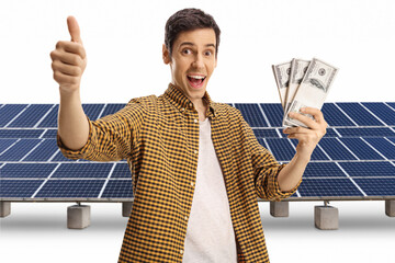 Poster - Happy young man holding stacks of money and gesturing a thumb up sign in front of solar panels