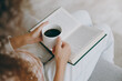 © ViDi Studio - Side view close up cropped fun young woman wear casual clothes sits on grey sofa couch reading book novel drink coffee stay at home hotel flat rest relax spend free spare time in living room indoor