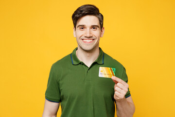 Poster - Young smiling cool cheerful caucasian happy man he wears green t-shirt casual clothes hold in hand mock up of credit bank card isolated on plain yellow background studio portrait. Lifestyle concept.