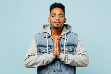 Sticker - Young man of African American ethnicity wear denim jacket orange t-shirt hold hands folded in prayer gesture, begging about something isolated on plain pastel light blue background. Lifestyle concept.