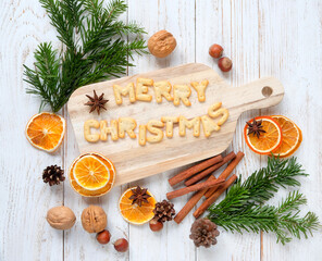 Sticker - Christmas holiday background. cutting board with Merry Christmas text made of cookies, cinnamon, orange slices, anise, nuts, cones, fir branches on white wooden table. winter festive season. top view