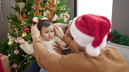 Wall Mural - Couple and son wearing reindeer ears sitting on sofa by christmas tree at home