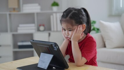 Wall Mural - Asian child girl serious to looking using and touch tablet display screen. Baby smiling funny time to use tablet. Too much screen time. Cute girl watching videos while tv, Internet addiction concept.