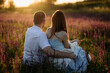 © sushytska - A young couple sits in a meadow with flowers and watches the sunset on a romantic picnic.