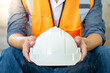 © Summer Paradive - Male worker wearing reflective orange vest holding white protective safety helmet while sitting at construction site