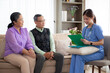 © NT_studio - Caregiver sitting on sofa checkup and diagnostic with elderly couple patient about health in living room at home, caretaker sitting on couch explaining and examining senior, insurance and medical.