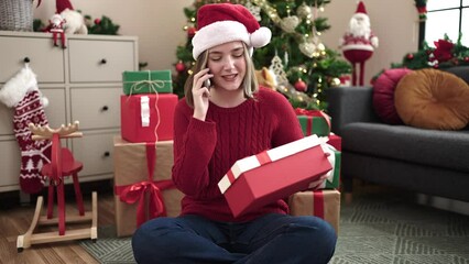 Poster - Young blonde woman talking on smartphone sitting on floor by christmas tree at home