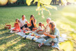 © Soloviova Liudmyla - Big family sitting on the picnic blanket in city park during weekend Sunday sunny day. They are smiling, laughing and eating boiled corn and watermelon. Family values and outdoors activities concept.