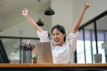 Female office worker expresses excitement at good news received on laptop screen, celebrates victory, excited about success