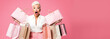 © OpticalDesign - A middle-aged hipster woman holding shopping bags, surprised face with mouth open, pastel pink background copyspace, low prices sale and discounts for black friday concept
