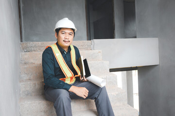 A foreman wearing a hard hat stands holding a blueprint. Supervising and inspecting the construction project of the building to be successful as planned.