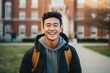 Smiling portrait of a young happy asian male student infront of a university