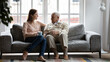 © fizkes - Happy elderly father sit on couch in living room talk with adult daughter drinking tea together, smiling senior dad and adult millennial girl enjoy family time weekend in retirement house or home