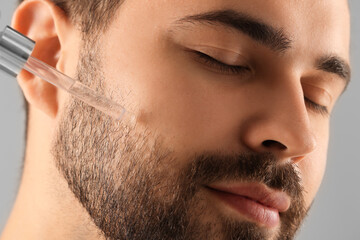 Poster - Handsome man applying cosmetic serum onto face, closeup