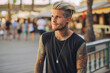 © MVProductions - Beautiful attractive young man with blonde hair and body and face tattoos. Enjoying outdoors at a lively boardwalk lined with shops and restaurants, emphasizing a carefree spirit