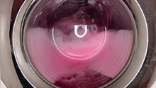 A Video Depicts A Washing Machine Drum In Which Faded Pink Clothes Are Being Washed, Resulting In The Foam Taking On A Vibrant Fuchsia Hue
