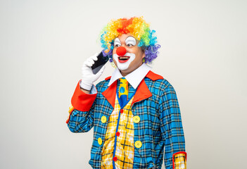 Wall Mural - Mr Clown. Portrait of Funny face Clown man in colorful uniform standing holding smartphone. Happy expression male bozo in various pose with cellphone on isolated background.