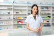 © Chanakon - Beautiful asian woman pharmacist checks inventory of medicine in pharmacy drugstore. Professional Female Pharmacist wearing uniform standing near drugs shelves counter