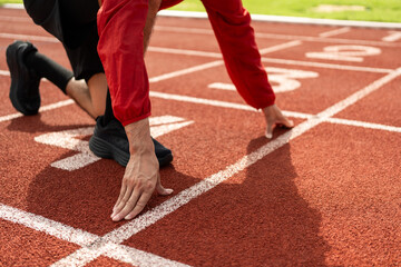 Young handsome indian man doing start pose before running exercise on track in sport stadium. Challenge race of athletes running in the starting point. Young asian man in sport athlete uniform