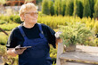 Senior woman gardener use computer tablet. Concept garden care service online