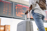 Fototapeta  - Travel on vacation. Woman passenger with suitcase is checking arrival and departure board schedule timetable at train or bus station