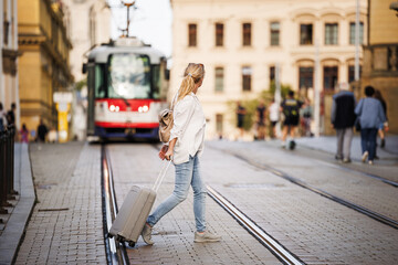 Wall Mural - Travel carefully and safety with insurance and avoid accidents. Woman tourist with suitcase walks across city street while tram arrives