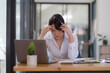 © amnaj - Young Asian woman feeling migraine head strain. Tired, Overworked businesswoman financier while working on laptop computer in office.