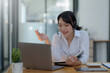 © amnaj - Happy young Asian student woman wearing headphones looking at webcam, looking at camera, during virtual meeting or video call talk.