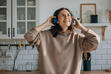 Happy woman wearing wireless headphones and listening to music in kitchen