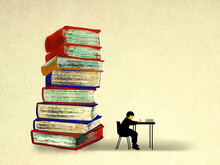 Stack Of Oversized Books Behind Boy Studying At Desk