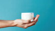 Round jar of cosmetic white cream in female hand isolated on flat blue background with copy space, product design template. 