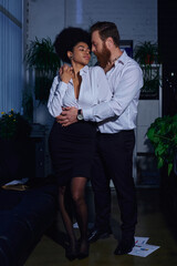 Wall Mural - full length of stylish interracial couple in formal wear embracing in office, romantic encounter