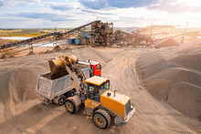 Aerial Top View Sand Quarry Industry. Yellow Excavator Loading Gravel To Truck, Sun Light