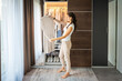 © dtatiana - Young woman with long curly dark hair standing in wardrobe and choosing old unwanted clothes for sale