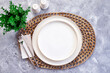 Simple dining table setting with white ceramic plate and silver cutlery over rattan round woven placemat  on wood background. top view, flat lay