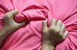 Closeup of a woman's hand holding a pink pillow on the bed.