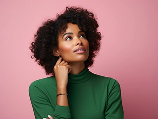 Wall Mural - Headshot portrait of thoughtful pensive young brunette woman with curly hair holding hand under chin looking upward against honeydew-green studio wall background with copy space for text advertisement