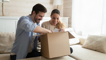 Happy Young Couple Unpacking Awaited Parcel At Home Together, Curious Man And Woman Looking Into Open Cardboard Box, Satisfied Customers Received Online Store Order, Good Delivery Service