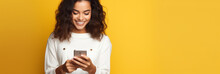 Latin woman wearing a white t-shirt and holding mobile phone looking at smartphone isolated on yellow background