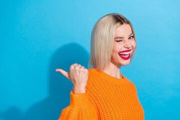 Photo of friendly cheerful girl wear knit orange jumper directing at product empty space blinking isolated on blue color background