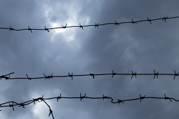 Tensioned barbed wire against a background of thick dark clouds