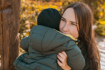 Wall Mural - Mother hugs her little asian son outdoors. Happy child walking in autumn park. Toddler baby boy wears trendy jacket and hat. Autumn fashion. Stylish child outside.