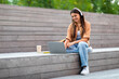© Prostock-studio - Positive young lady hipster using laptop and headphones outdoors