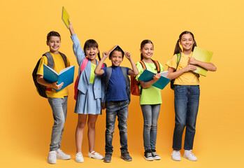  Cheerful multiracial school kids with backpack and books on yellow