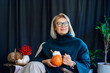 © okrasiuk - Smiling middle aged woman relaxing with pumpkin shaped cup of hot drink with whipped cream and cinnamon stick with fall mood composition for hygge home decor on background. Cozy autumn holidays